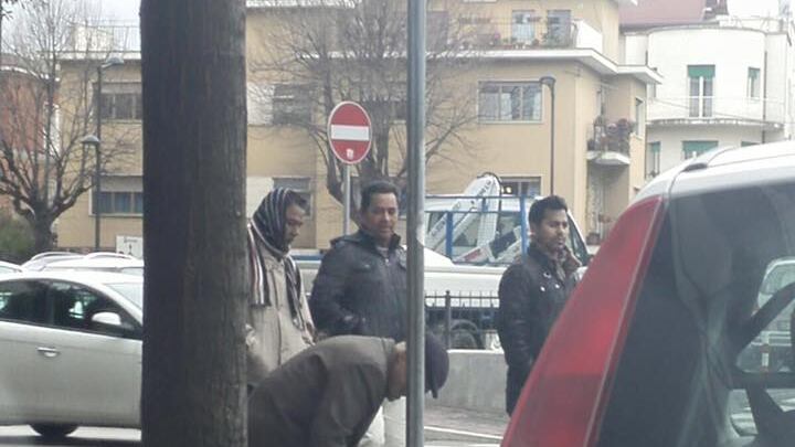 Le mani dell'anziano cercano tra i rifiuti E i migranti guardano