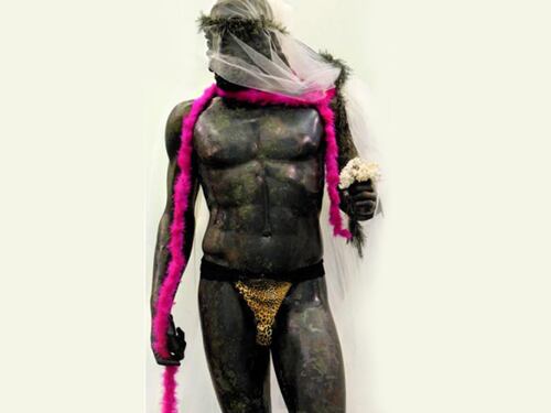 I Bronzi di Riace fotografati con tanga, boa fucsia e velo